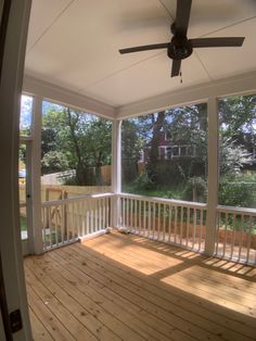 an empty porch with a ceiling fan and wooden flooring in front of the windows