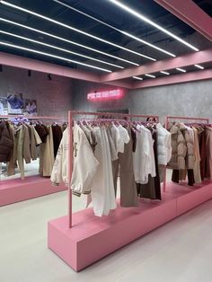 clothes are hanging on racks in a clothing store, with pink lighting above the rack