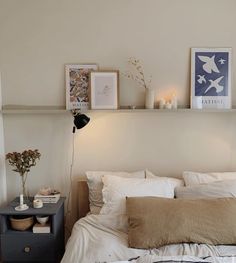 a bed with white sheets and pillows in a bedroom next to two framed pictures on the wall