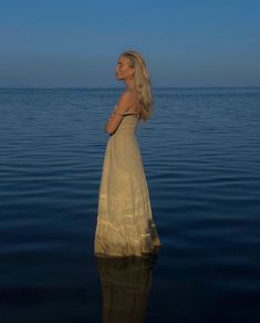 a woman standing in the water with her back to the camera looking at the sky