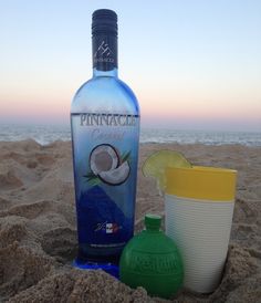 a bottle of ginzaccle next to a cup on the sand at the beach