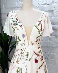 a white dress with red and green flowers is on display in front of a brick wall