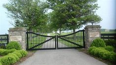 a gated driveway leading into a grassy area with trees and bushes on either side