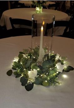 a candle that is on top of a table with flowers and greenery around it