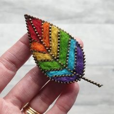 a hand holding a colorful brooch with beading on it's back and side