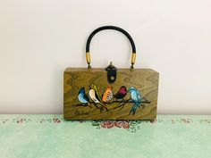 a wooden purse with colorful birds painted on it's front and back sides, sitting on a table