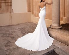 a woman in a white wedding dress leaning against a pillar