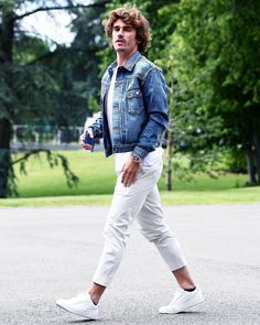 a man walking down the street in white pants and a denim jacket with his hand on his hip