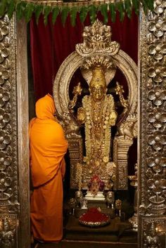 a person standing in front of a gold statue with an orange robe on it's head