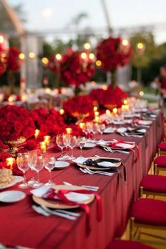 a long table is set with red flowers and candles