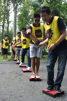 a group of young men standing on top of skateboards in a park with trees behind them