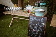 a picnic table with wine glasses and bottles on it, next to a chalkboard sign