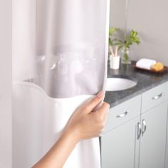 a person is opening the shower curtain to look at their bathroom sink and countertop