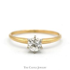 a yellow gold engagement ring with a round diamond in the center, on a white background