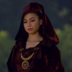 a woman wearing a red cloak and gold necklace