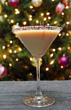 a glass filled with liquid sitting on top of a table next to a christmas tree