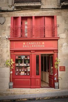 a store front with red shutters and flowers in pots on the window sill