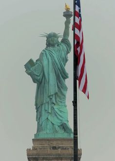 the statue of liberty is holding an american flag in front of it's base