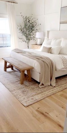 a bedroom with white walls and wood flooring has a bench in the middle of the bed