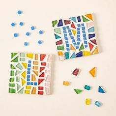 two pieces of colorful mosaic tile next to each other on a white surface with colored glass shards scattered around them