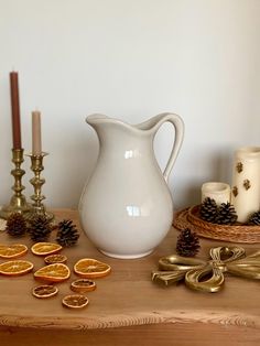 a white pitcher sitting on top of a wooden table next to candles and orange slices