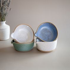 three ceramic dishes and a vase with lavender in the background on a table top,