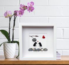 a vase with flowers and rocks in it sitting next to a white framed wall hanging