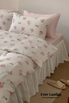 a bed with white sheets and pink flowers on it, next to two slippers