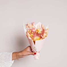 a hand holding a bouquet of flowers on a white background with pink and yellow colors