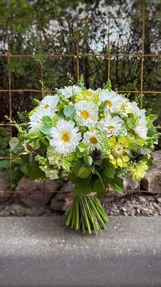 a bouquet of white and green flowers in front of a metal fence with trees behind it