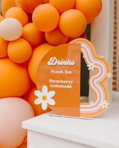 an orange sign sitting on top of a white table next to balloons and flowers in the background