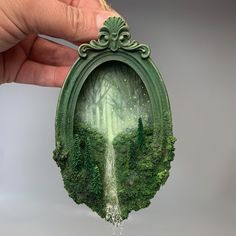 a hand holding up a small piece of art that looks like a forest with trees in it