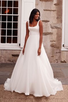 a woman in a white wedding dress standing on the sidewalk near a stone wall and windows