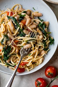 pasta with spinach, tomatoes and chickpeas is served in a white bowl