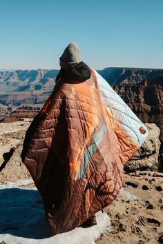 a man sitting on top of a mountain covered in a blanket and looking out over the canyon