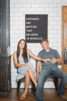 a man and woman sitting next to each other in front of a sign