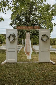 a wedding dress hanging in front of an outdoor ceremony area with wreaths on the doors