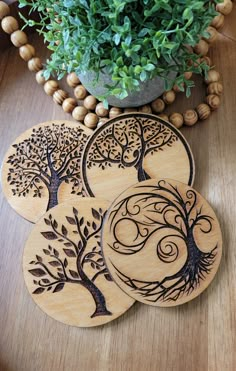 four wooden coasters with tree designs on them sitting next to a potted plant