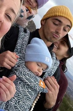 a group of people standing next to each other with a baby in a carrier on top of a mountain