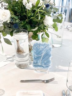 there is a vase with white flowers on the table next to a card and silverware