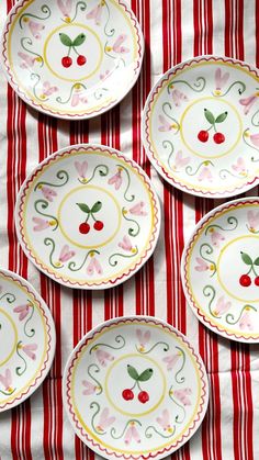 four plates with cherries on them sitting on a red and white striped tablecloth