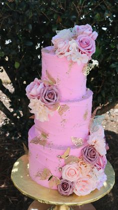 a three tiered cake with pink and gold flowers on the top is sitting on a golden pedestal