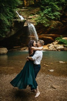 a man and woman hug in front of a waterfall while they stand on the ground