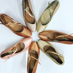 several pairs of ballet shoes arranged in a circle on a white surface, with the bottom part showing