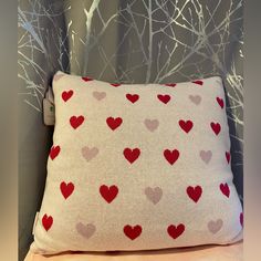 a white pillow with red and grey hearts on it sitting on a bed next to a tree