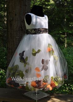 a dress made out of tulle and fabric with butterflies on the skirt is sitting in front of a tree