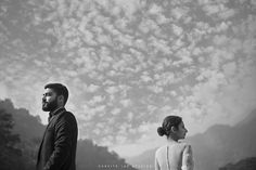 a man and woman standing next to each other in front of a sky with clouds