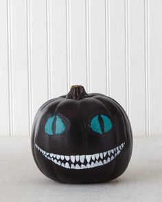 a black pumpkin with blue eyes and fangs on it's face is sitting in front of a white wall