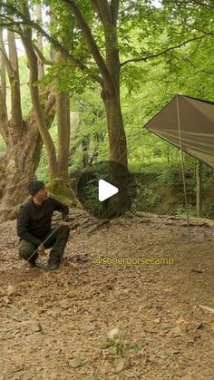 a man kneeling down in the woods next to a tent with a tarp on it