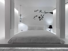 a bedroom with white walls and flooring has a bed in the middle, two lamps on either side